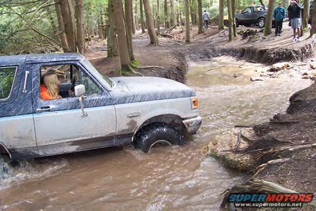 1991 Ford Bronco driving through water on a wooded trail