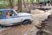 1991 Ford Bronco - A 1991 Ford Bronco navigates a muddy water crossing on a wooded trail, with other vehicles and people visible in the background.
