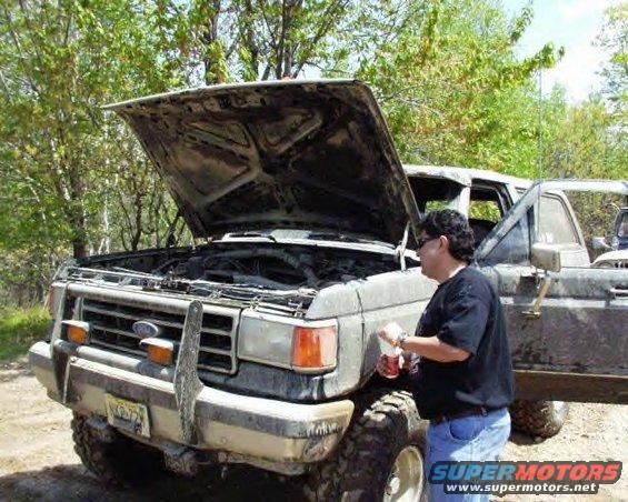 1987 Ford F-Series truck, hood open, person standing by engine. Muddy exterior