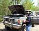 1991 Ford Bronco - Person checks engine of a muddy 1987 Ford F-Series truck with hood open.