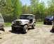 1991 Ford Bronco - A vintage Jeep CJ-5 is parked on a dirt path, with other vehicles visible in the background.
