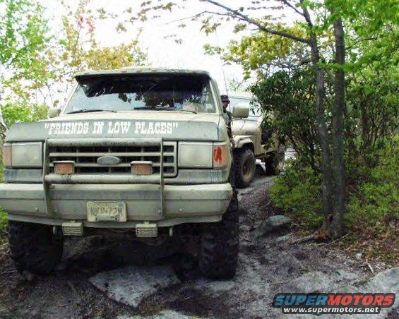 Tan 1987 Ford Bronco with a brush guard and "Friends in Low Places" text on the windshield