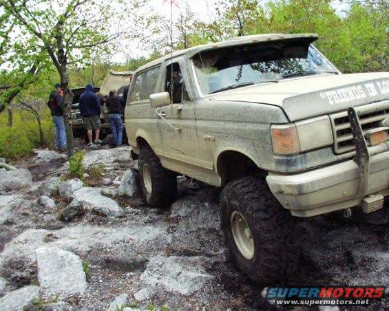 Muddy 1991 Ford Bronco on rocky terrain with people around another vehicle