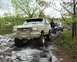 1991 Ford Bronco - Two trucks are shown off-roading on a rocky path with trees and foliage surrounding them.