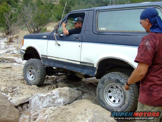 Two-tone Ford Bronco navigating rocky terrain with a driver and observer