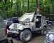 1991 Ford Bronco - A man works on a camouflaged Jeep CJ-7 with its hood open, parked in a wooded area.