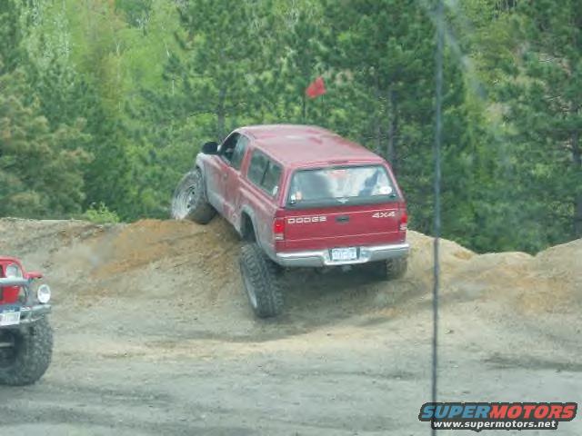 Red Dodge SUV with a cap is climbing a dirt hill. Another red Jeep is visible on the left
