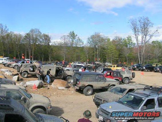 Off-road vehicles parked in a dirt lot with trees in the background