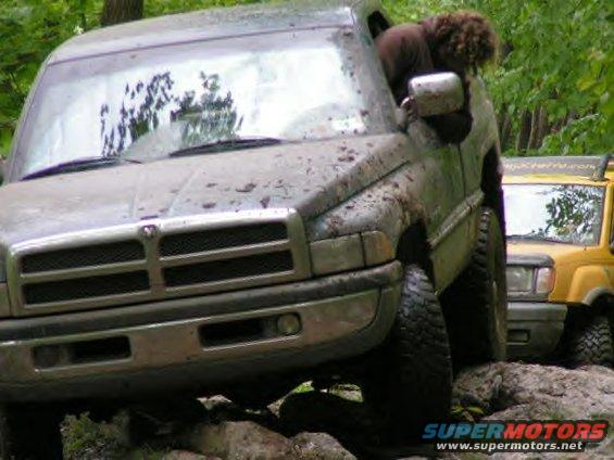 Muddy Dodge Ram pickup truck on rocks, another yellow vehicle behind it