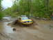 1991 Ford Bronco - This yellow SUV navigates a muddy off-road trail, kicking up a large spray of mud.