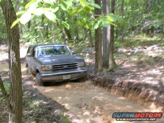 1991 Ford Bronco navigating a muddy path in a forest