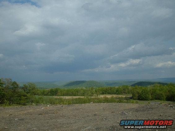 Dirt foreground with distant green hills and cloudy sky