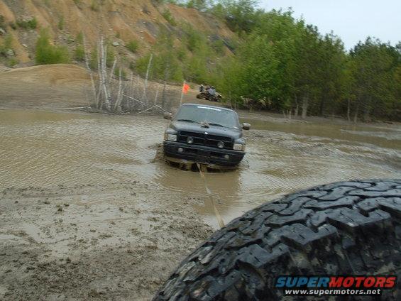 Black Dodge Ram truck stuck in mud, another vehicle and ATV in background