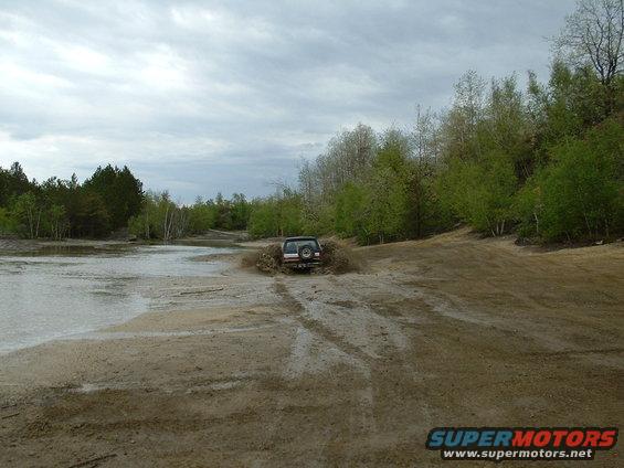 SUV kicking up mud and water while driving through a muddy area with trees and a cloudy sky