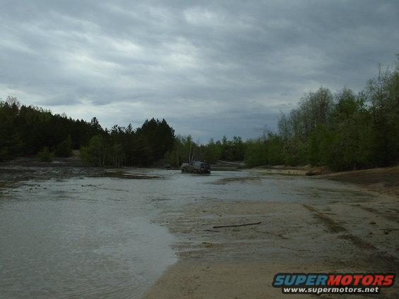 SUV driving through shallow water with trees in background