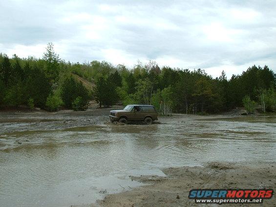 Brown 1991 Ford Bronco driving through a muddy field