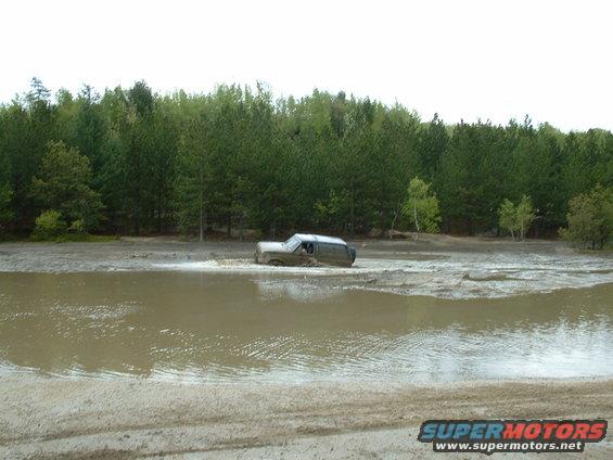 SUV driving through muddy water with trees in background