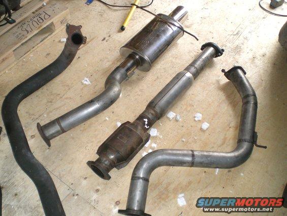 Exhaust pipes and muffler laid out on a wooden floor