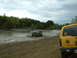 1991 Ford Bronco - A brown SUV navigates a muddy off-road course, while a yellow SUV is parked nearby.