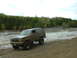 1991 Ford Bronco - 1991 Ford Bronco navigates a muddy off-road course with a forest backdrop.