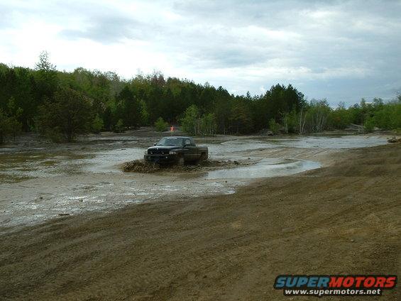 Dark pickup truck driving through mud, orange flag on antenna
