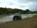 1991 Ford Bronco - A black pickup truck navigates a muddy terrain under a cloudy sky.