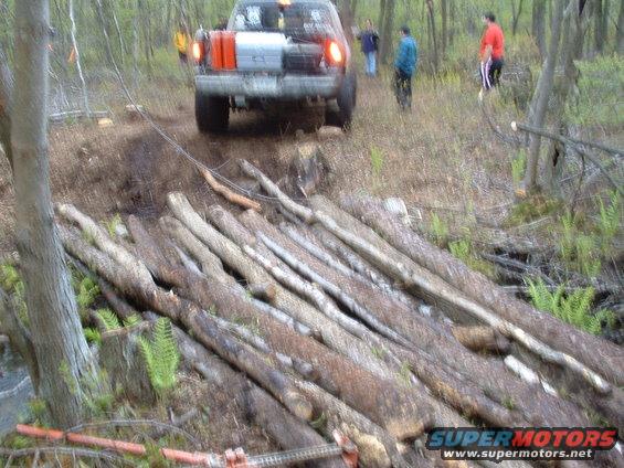 Rear view of a 1991 Ford Bronco driving over a log bridge in a forest