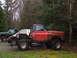 1976 GMC Sierra 2500 - A heavily modified red pickup truck sits in a wooded area next to another pickup and a car.