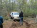 1991 Ford Bronco - A silver SUV drives through a wooded area on a dirt path, with a person standing nearby.