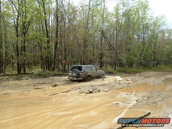 Ford Bronco driving through a muddy trail in the woods