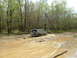 1991 Ford Bronco - A Ford Bronco navigates a challenging muddy off-road path surrounded by trees.