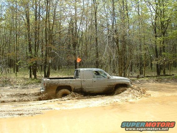 Mud-covered pickup truck struggling through a muddy trail in a wooded area