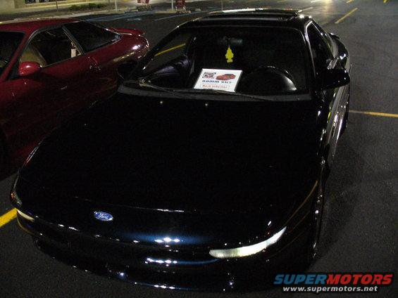 Dark blue coupe with a sunroof, parked next to a red car. A sign is on the dashboard
