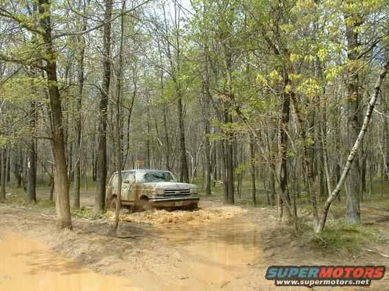 Mud-splattered 1992 Ford Bronco driving through a muddy forest path