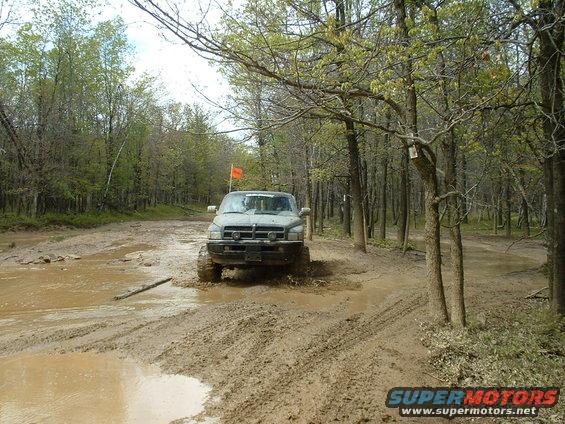 Truck driving through mud on a wooded trail with an orange flag on top