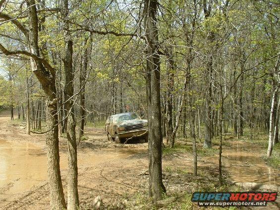 Mud-covered 1987 Ford Bronco driving through a muddy wooded area