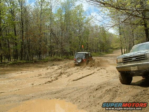 1991 Ford Bronco and another SUV driving through mud on a dirt road
