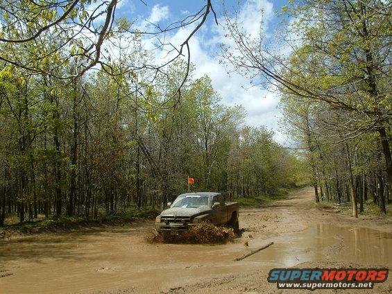 Mud-splattered truck driving through a muddy road with trees on both sides