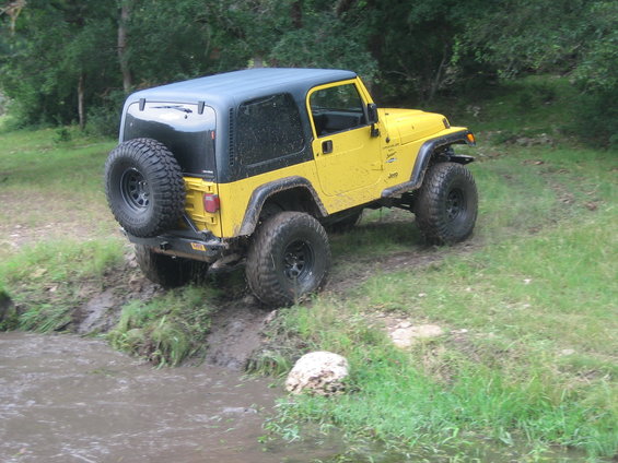 Yellow Jeep Wrangler with black top driving through mud and water