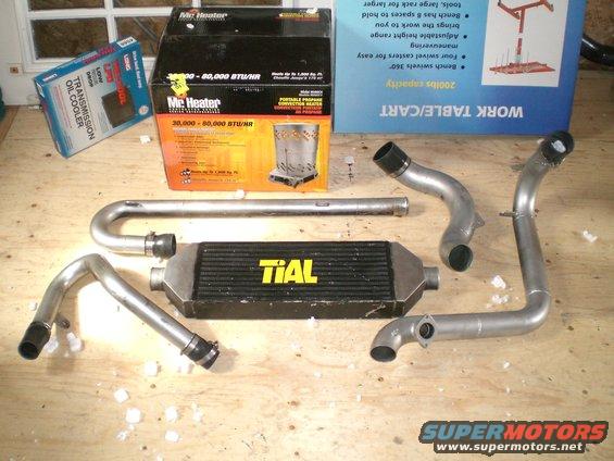 Intercooler with TIAL branding, along with several bent metal pipes and a transmission oil cooler box
