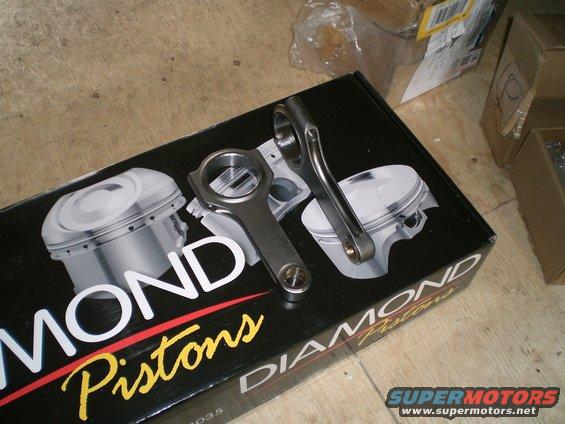 Two engine connecting rods resting on a box with "Diamond Pistons" printed on it, showing an illustration of pistons