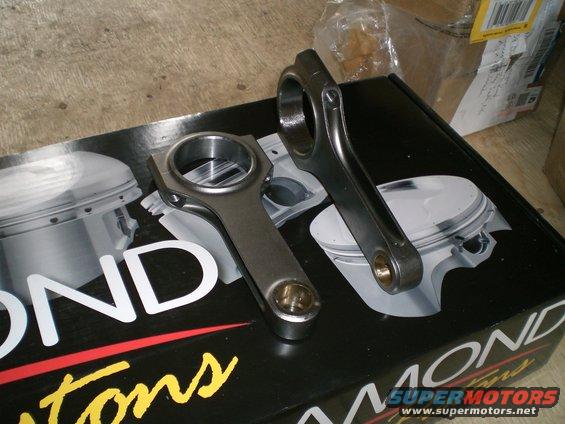 Two metal connecting rods resting on a black box with piston diagrams and text