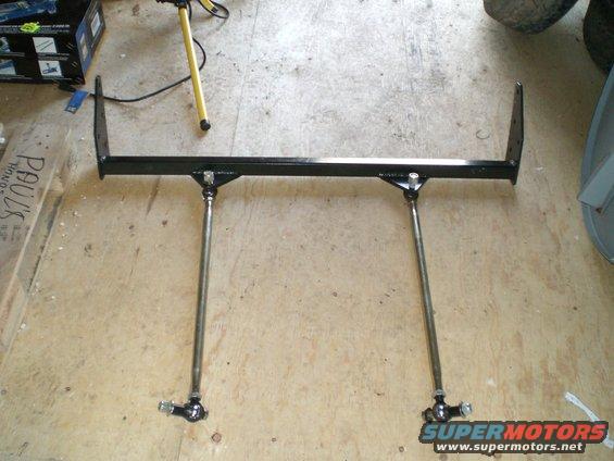 Black metal traction bars with adjustable rods and ball joints, lying on a concrete floor