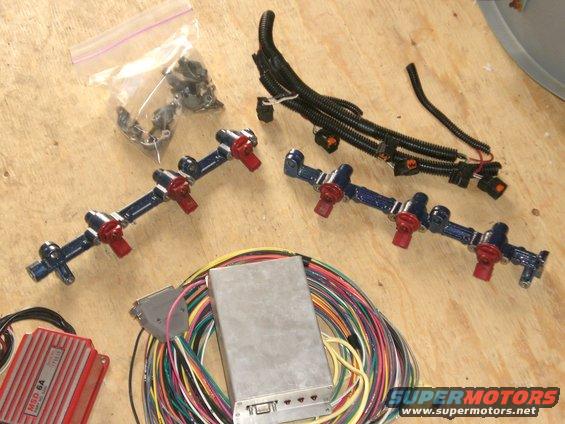 Modified fuel rails with red injectors and wiring harness on a wooden surface