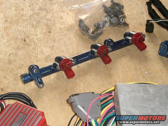 Blue fuel rail with red-top injectors, wiring harness, and electronic control unit on a wooden surface