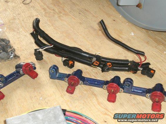 Blue fuel rails with red injectors and black wiring harnesses on a wooden surface