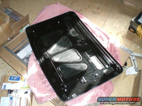 underside of a black car hood, possibly for a 1995 Ford Probe, resting on a pink blanket with boxes around it