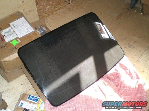 Carbon fiber moonroof panel with visible weave pattern, resting on a red cloth
