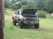 2001 Jeep Wrangler - A camouflaged pickup truck sits in a grassy field with its hood open, revealing the engine compartment.