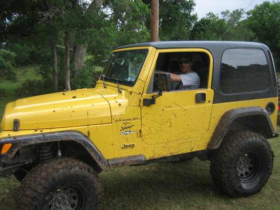 Yellow Jeep Wrangler with a man driving. It's covered in mud